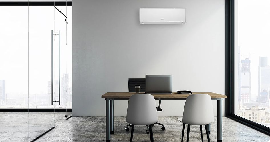 Nowoczesne biuro z drewnianym biurkiem i dwoma krzesłami naprzeciwko laptopa. Szklana ściana po lewej stronie, a duże okno pokazuje panoramę miasta. Wydajna jednostka Klimatyzacja Gree jest zamontowana na szarej ścianie nad biurkiem, zapewniając komfort w godzinach pracy.