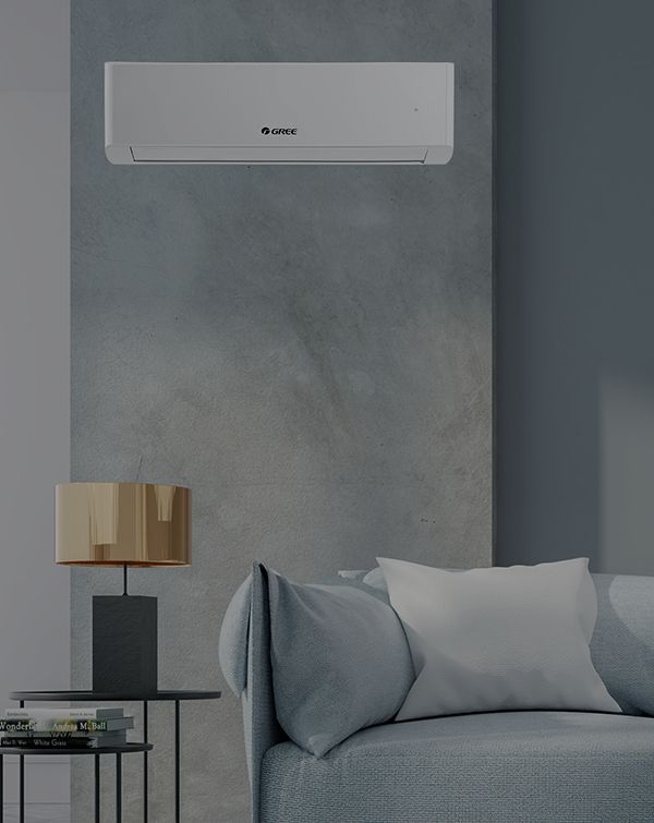 Nowoczesny salon ma elegancką białą jednostkę klimatyzacyjną zamontowaną na szarej ścianie. Poniżej znajduje się jasnoszara sofa z białymi poduszkami i mały stolik ozdobiony złotą lampą i stosem książek.